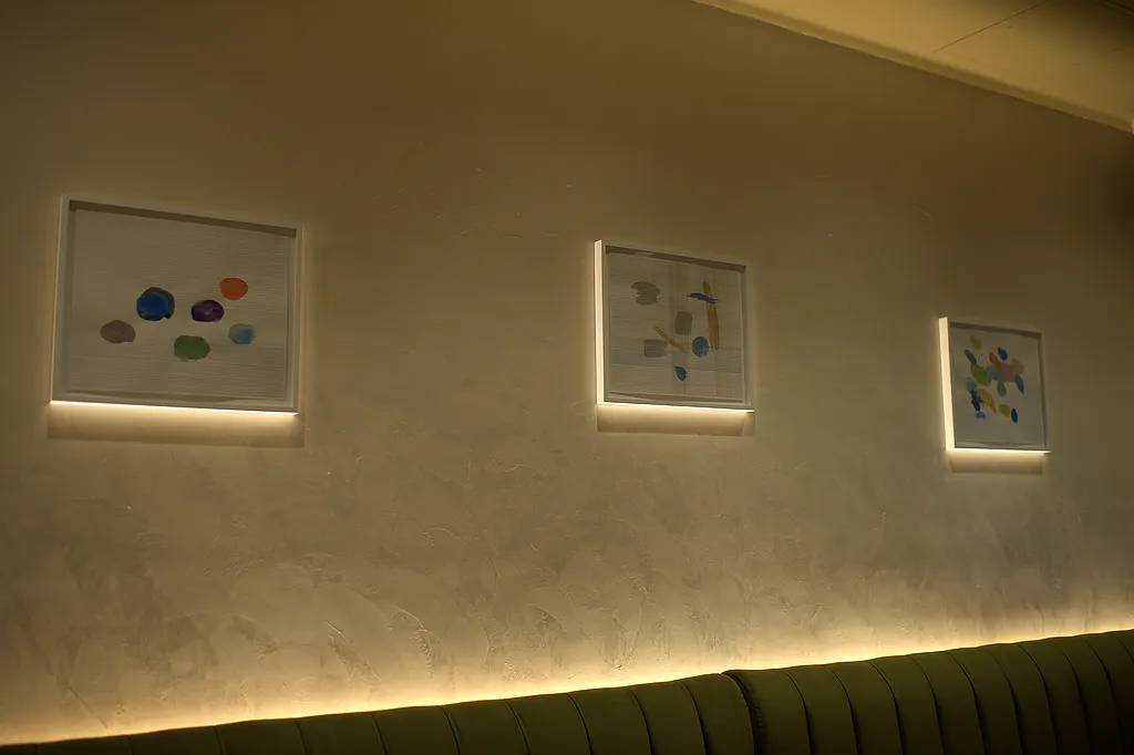 Framed works lit against a plaster wall above the banquette